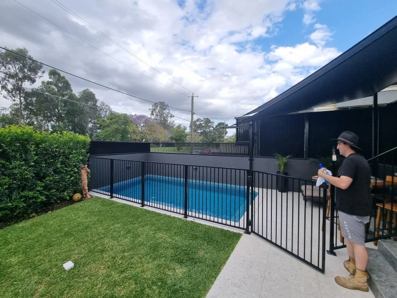 Man standing next to pool gate and green grass