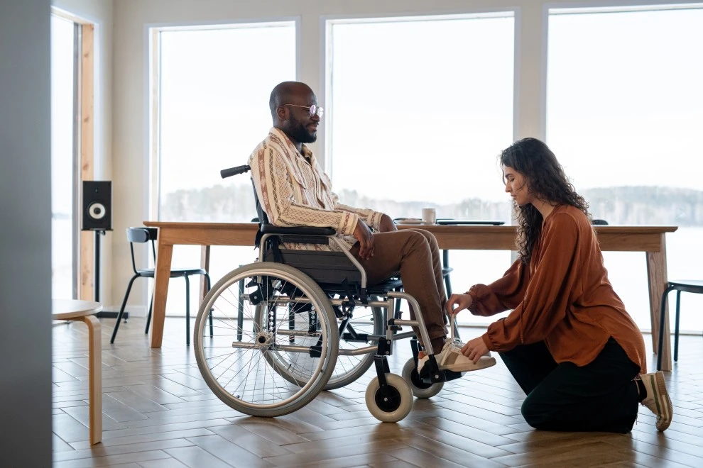 Support worker putting on disabled man in wheelchair's shoes