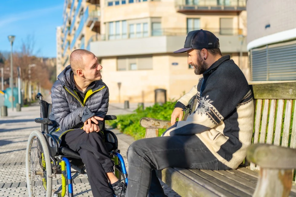 Disabled man in wheelchair talking with support worker outside